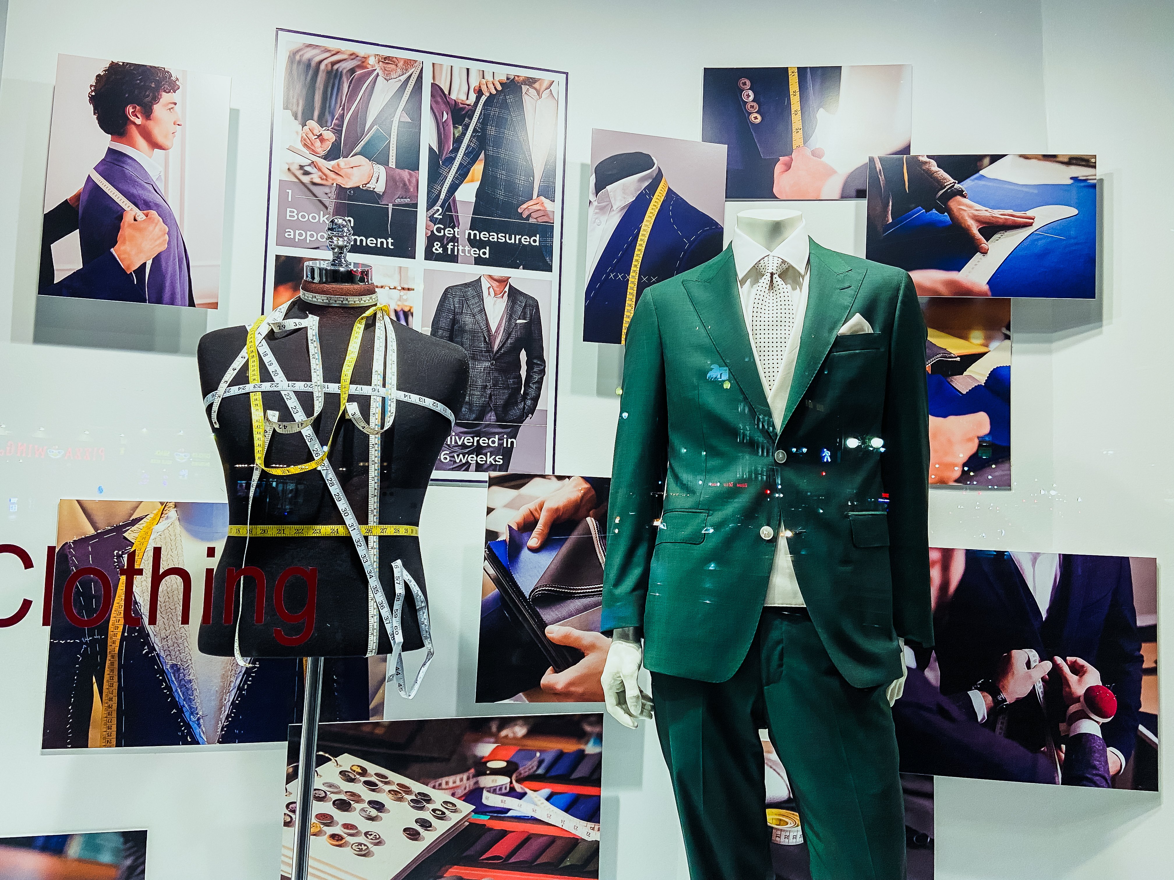 A store display advertises custom tailoring services, prominently displaying measuring tape, and a mannequin with a green suit.