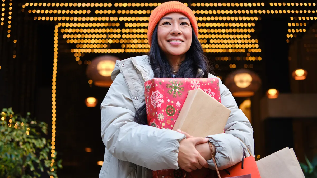 A person wearing a knit cap and winter coat carrying a bunch of shopping bags and holiday gifts.