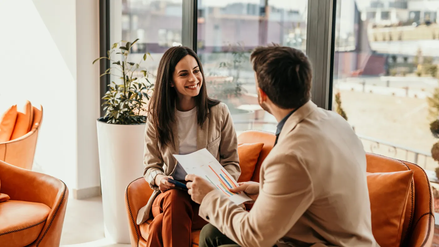 Two colleagues discuss colorful bar graphs in a modern office lounge.