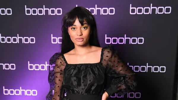 A person with dark hair in front of a wall that says "boohoo" repeatedly.