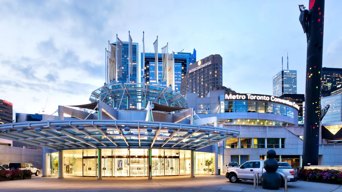 A rounded, glass building that says "Metro Toronto Convention Centre" at dusk in front of the Toronto skyline.