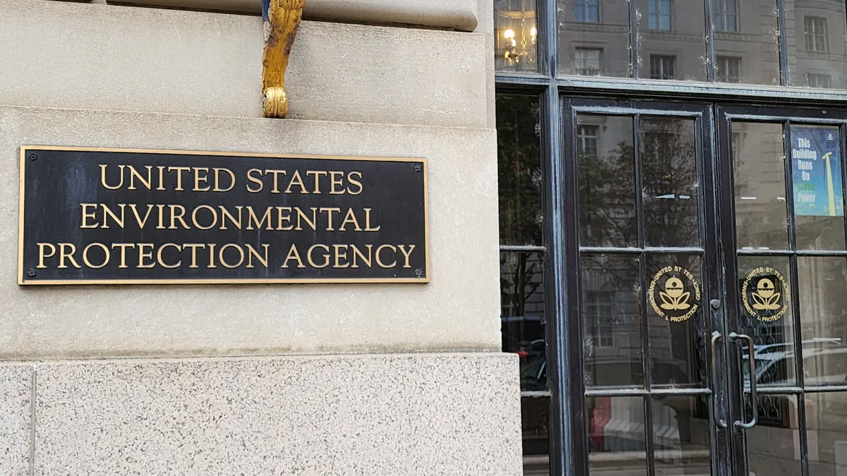 A black U.S. Environmental Protection Agency sign on a tan building and placed next to glass double-doors.