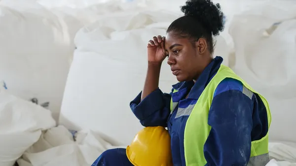 Young tired female engineer or worker of warehouse sitting by heap of huge white sacks with raw materials