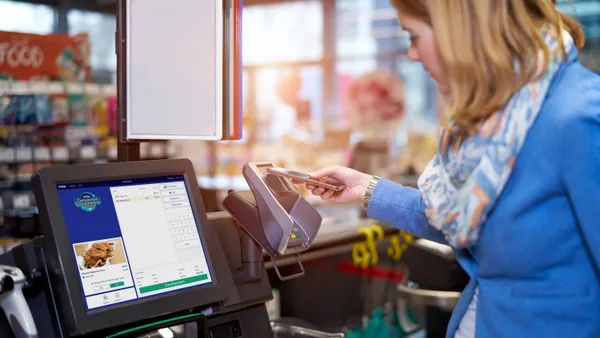 A photo of a person using their phone to pay for purchases at a self-checkout kiosk.