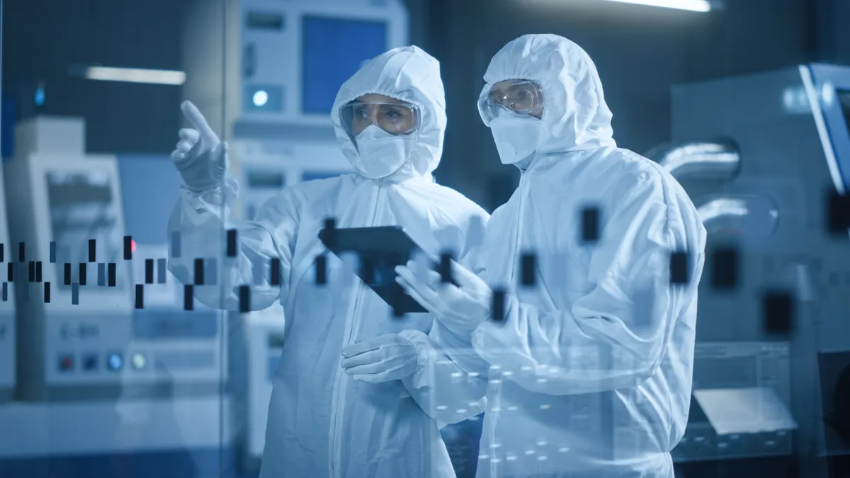 Two employees discuss findings on a tablet in a factory cleanroom.