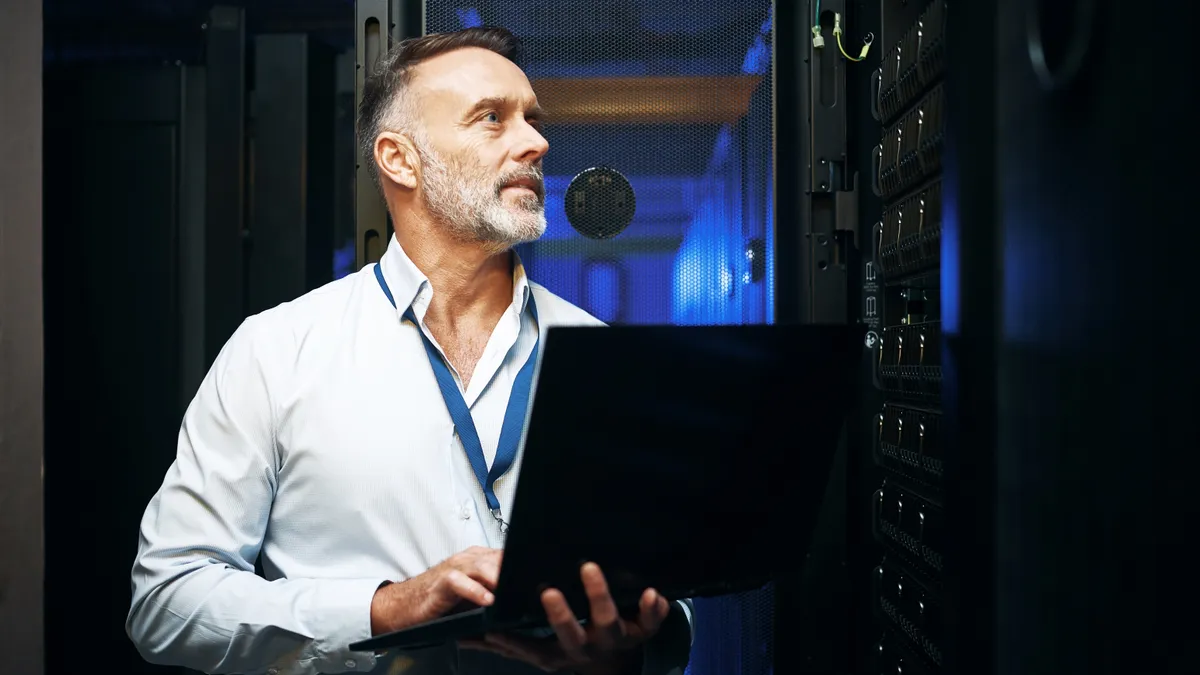 Shot of a mature man using a laptop while working in a server room.