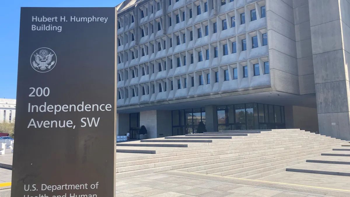 A sign for the U.S. Department of Health and Human Services stands outside of a concrete building.