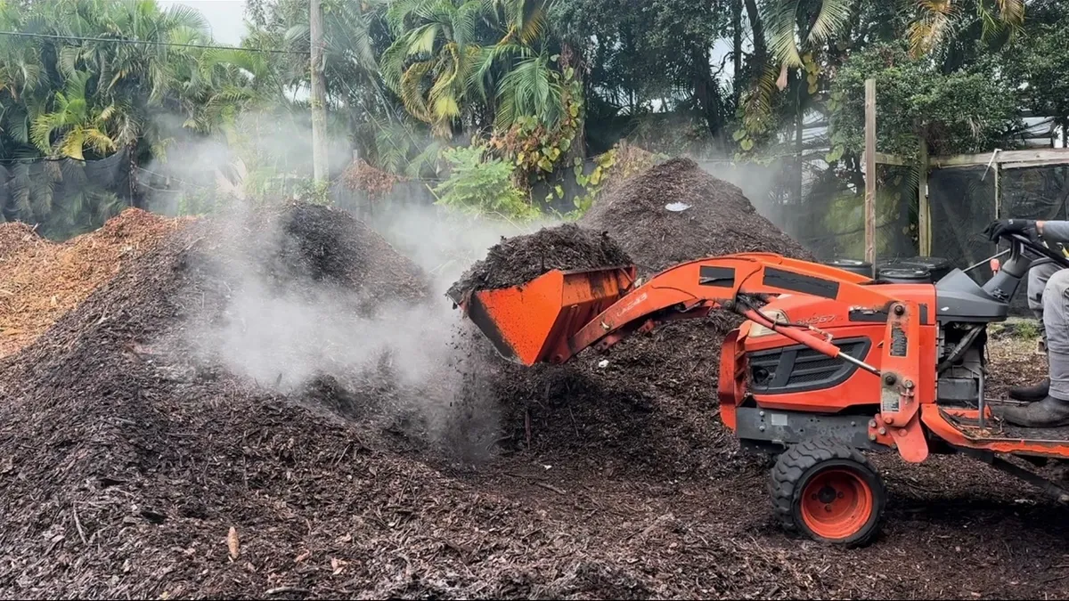 A piece of heavy equipment manages a steaming compost pile