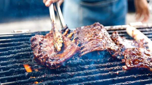 Close up photo of a chef grilling meat with tongs.