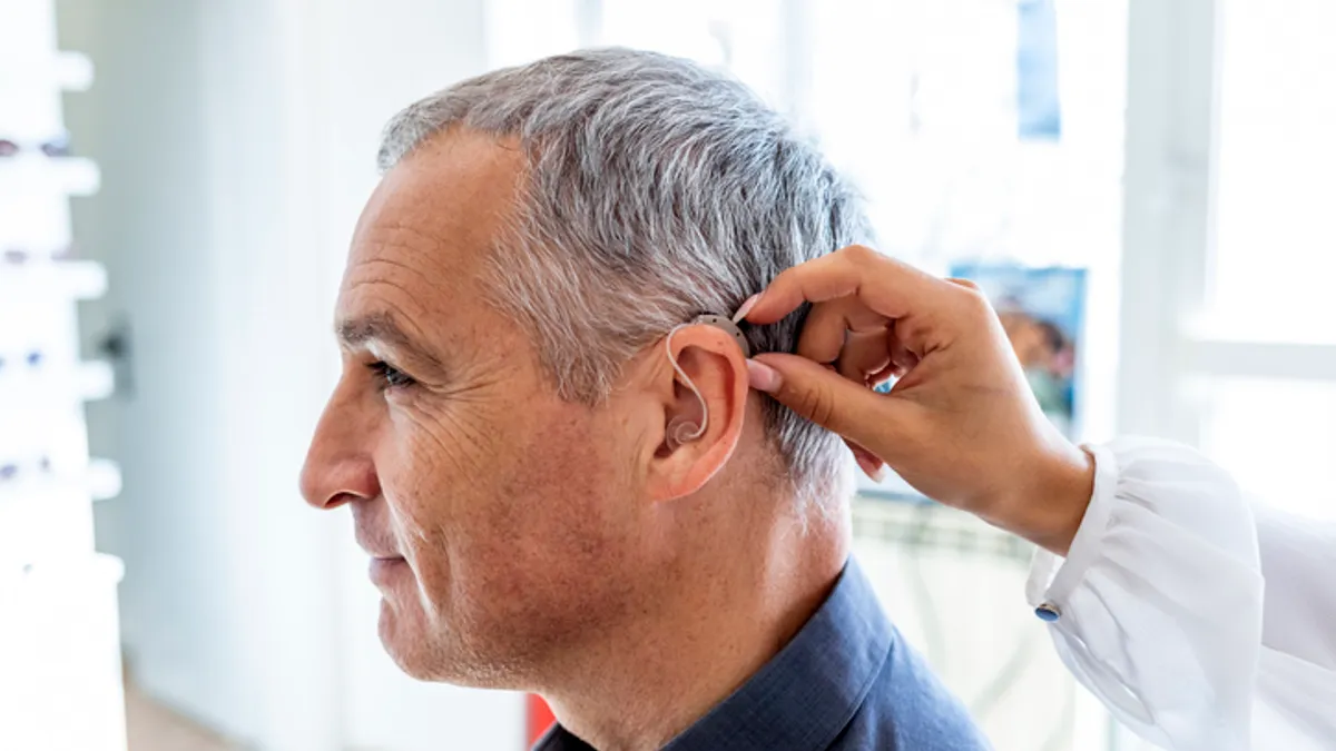 A doctor places a hearing aid in a person's ear.