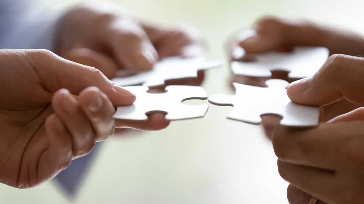 Close up hands of four businesspeople hold pieces of white puzzle