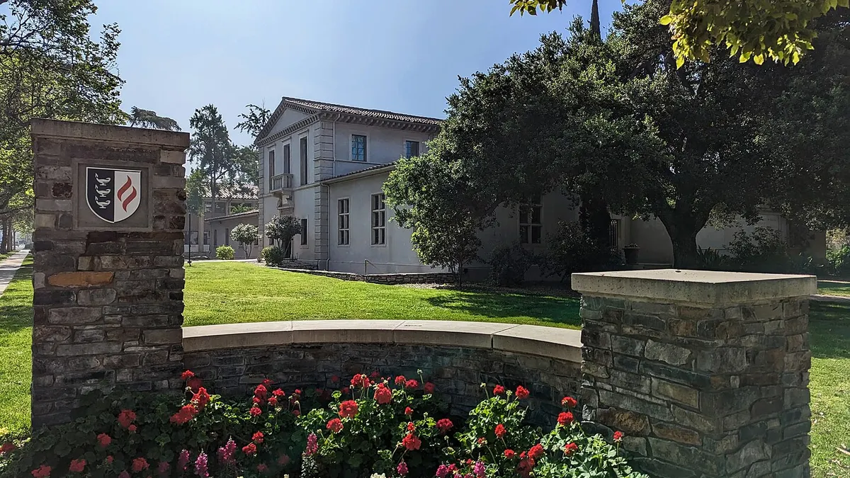 Stone wall in foreground with stucco Spanish-style building in background.