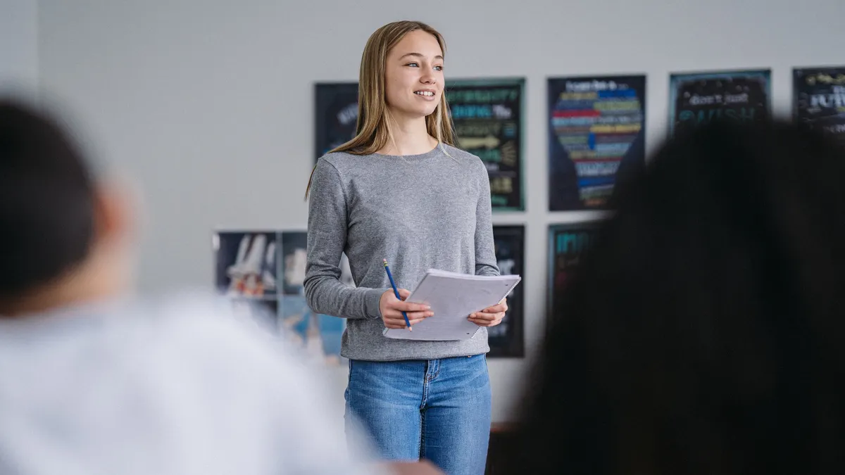 A teenage girl stands in front of her middle school class to present information.