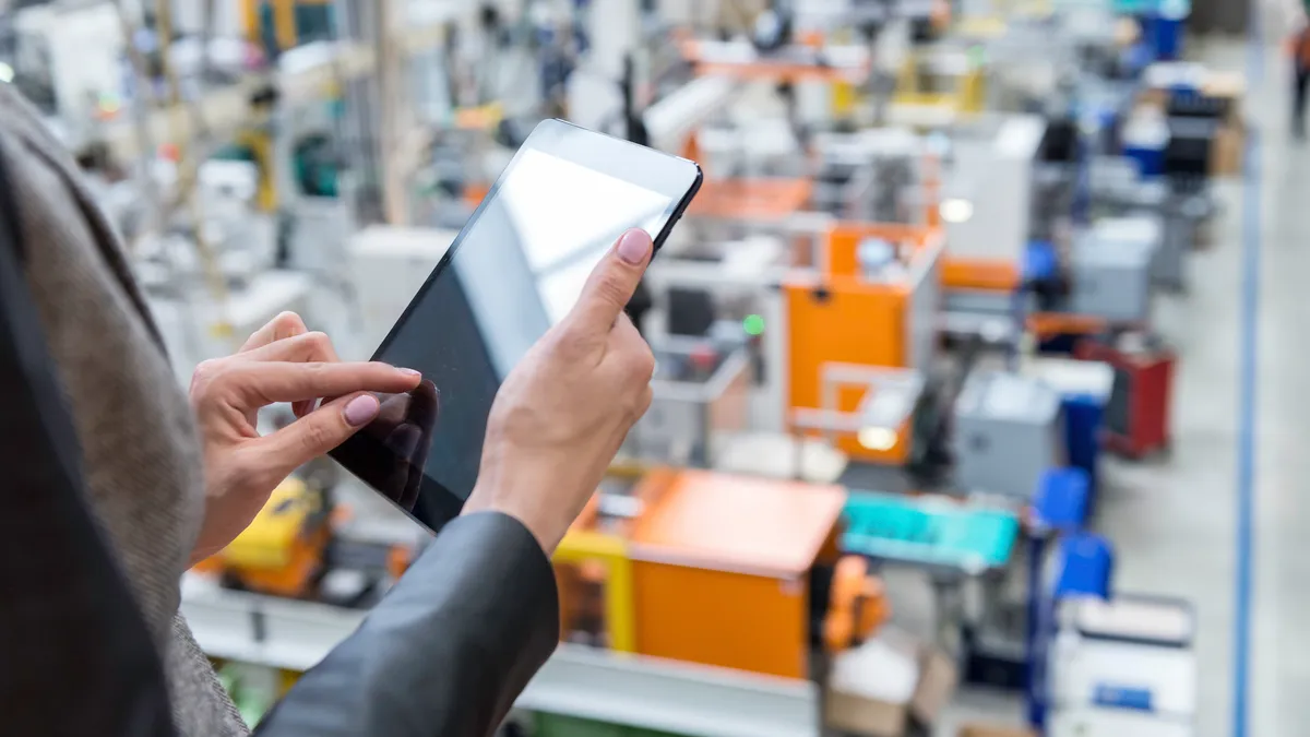 Horizontal color image of businesswoman - unrecognizable person - working with digital tablet in large futuristic factory. Woman