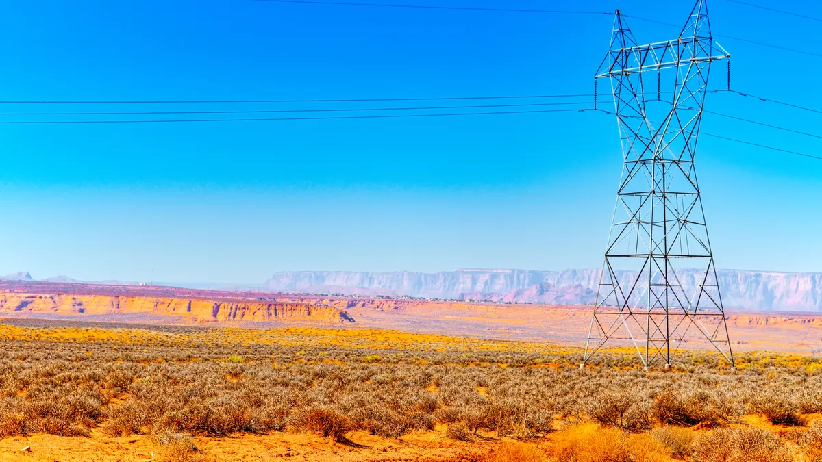 Electric power lines cross a scrubby desert with a mesa in the background.