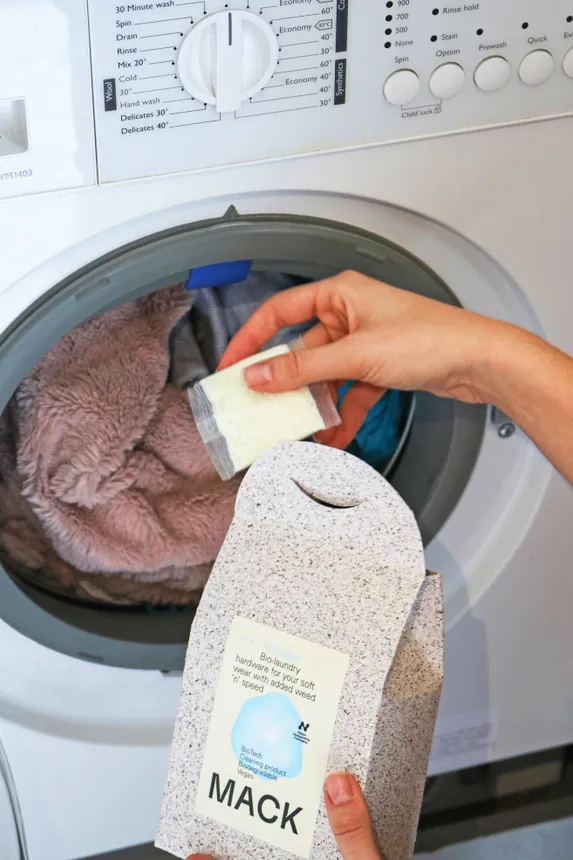 A person puts a seaweed-derived detergent pouch in a washing machine