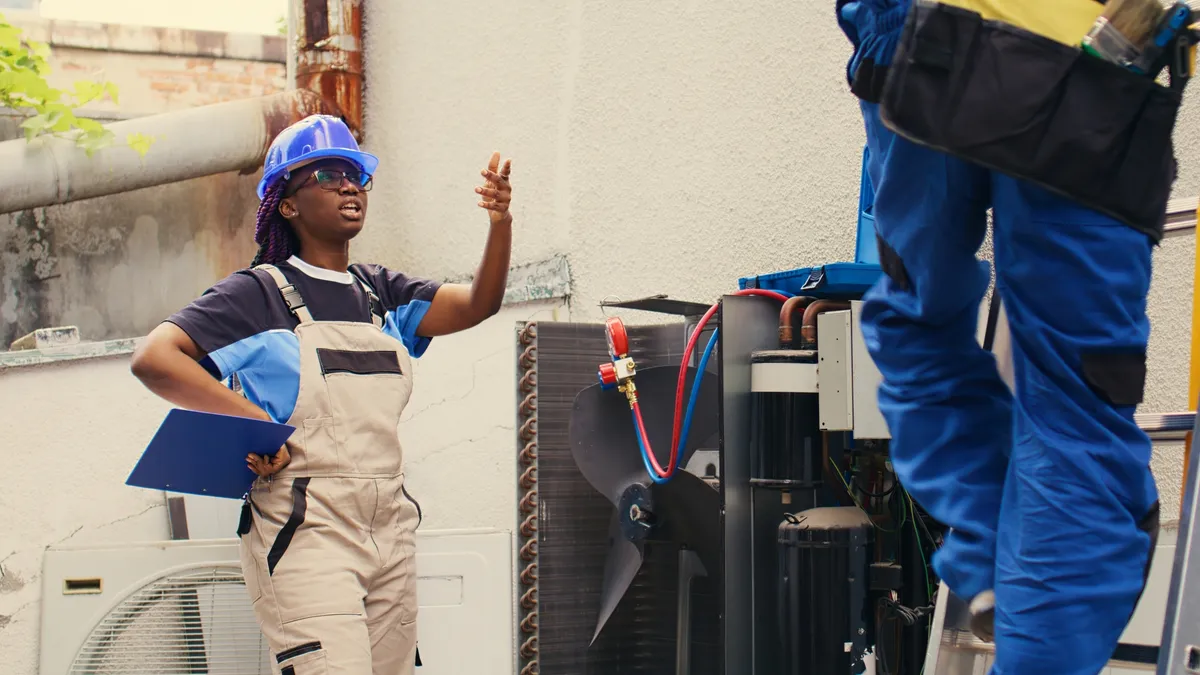 A student talks with a training instructor to fix an outdoor air conditioner.