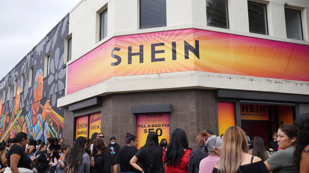 Customers gather outside a corner concrete store with a banner across the front that reads Shein