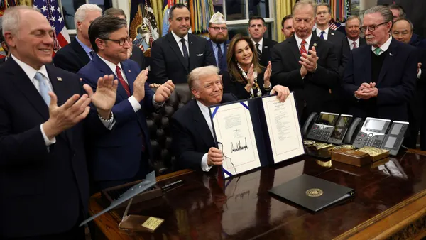 A group of people around President Donald Trump, who holds up a signed bill.