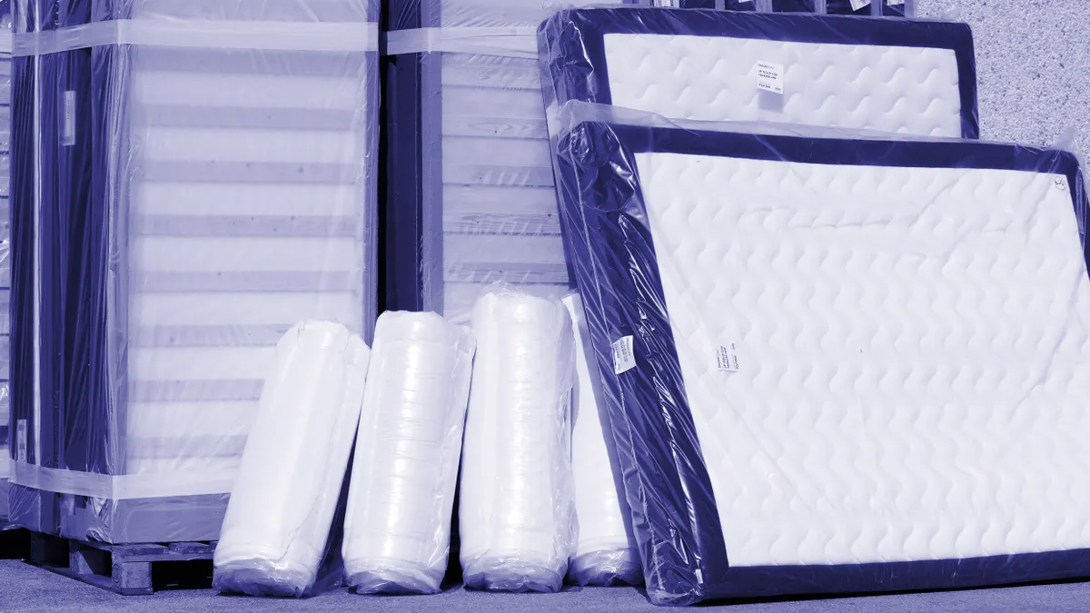 Baseboards and mattresses wrapped in plastic are stacked against a building wall.