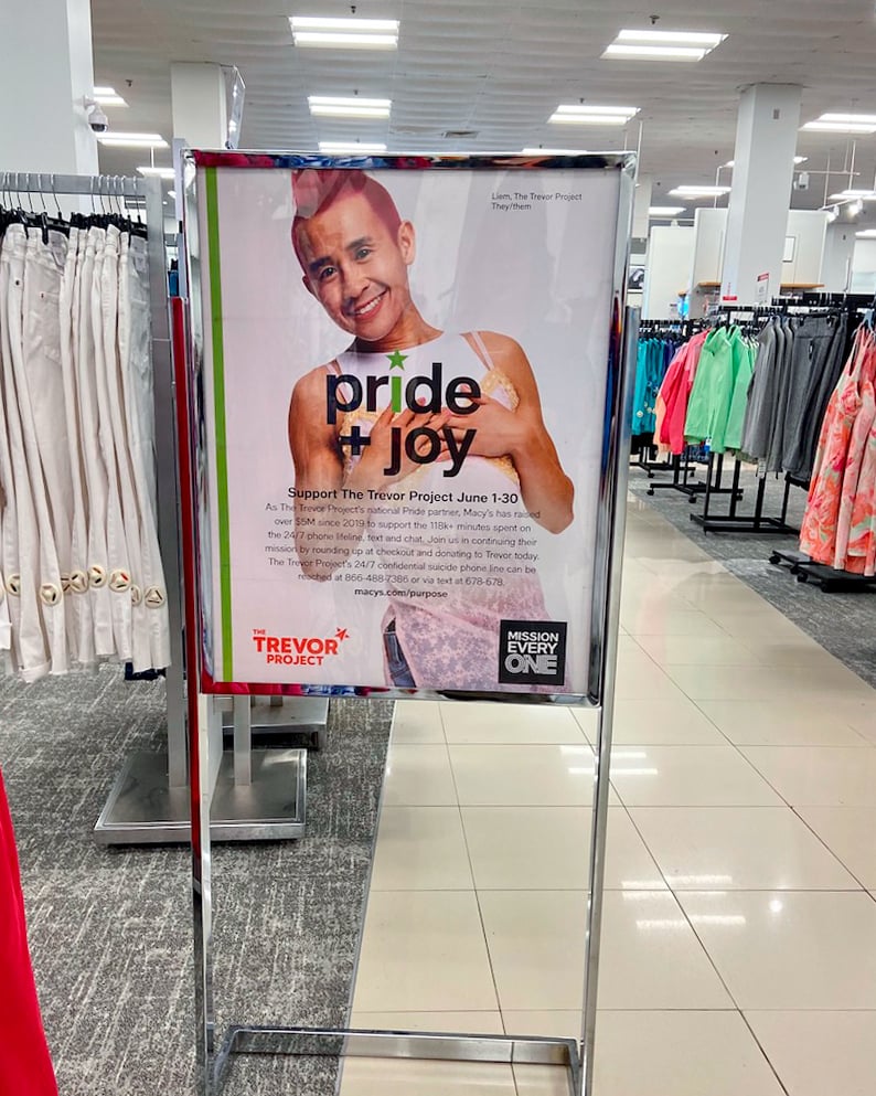 A sign advertising the Trevor Project is placed among racks of apparel.