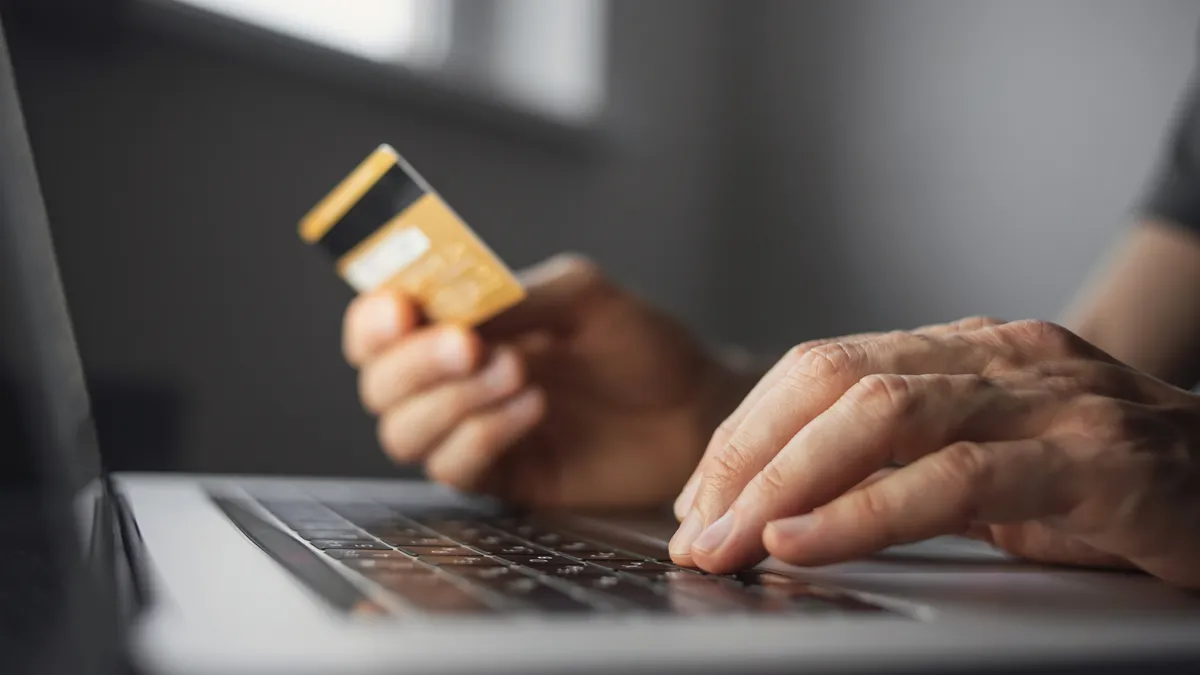 A person holds a credit card in front of a laptop computer.