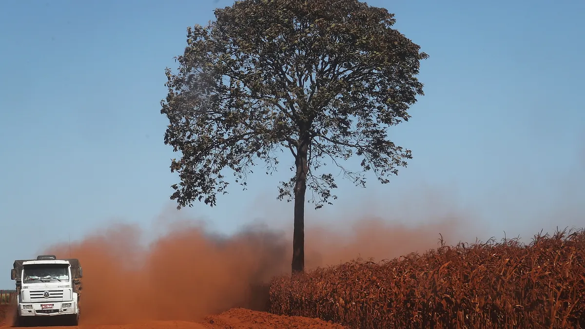 A truck kicks up dirt as it passes a farm field in a deforested section of the Amazon