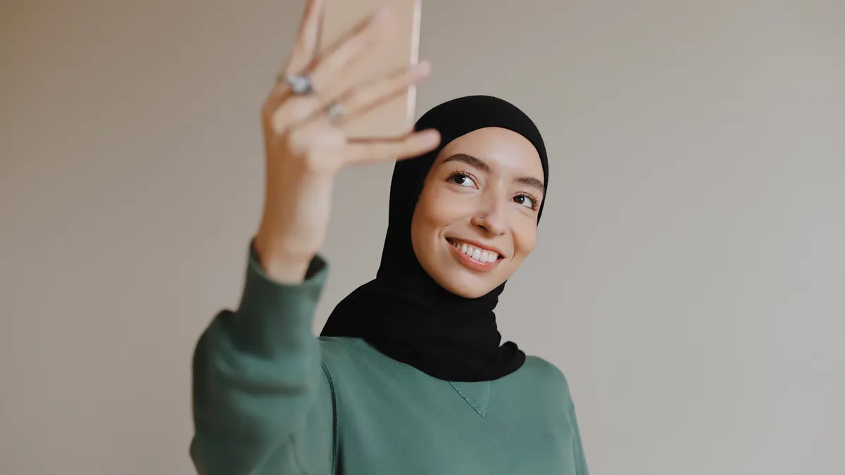 A hijabi person smiles while taking a selfie