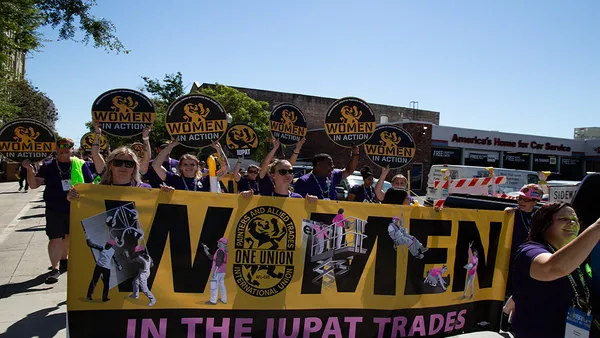 Group of people holding a 'Women in the IUPAT Trades' banner at an event.