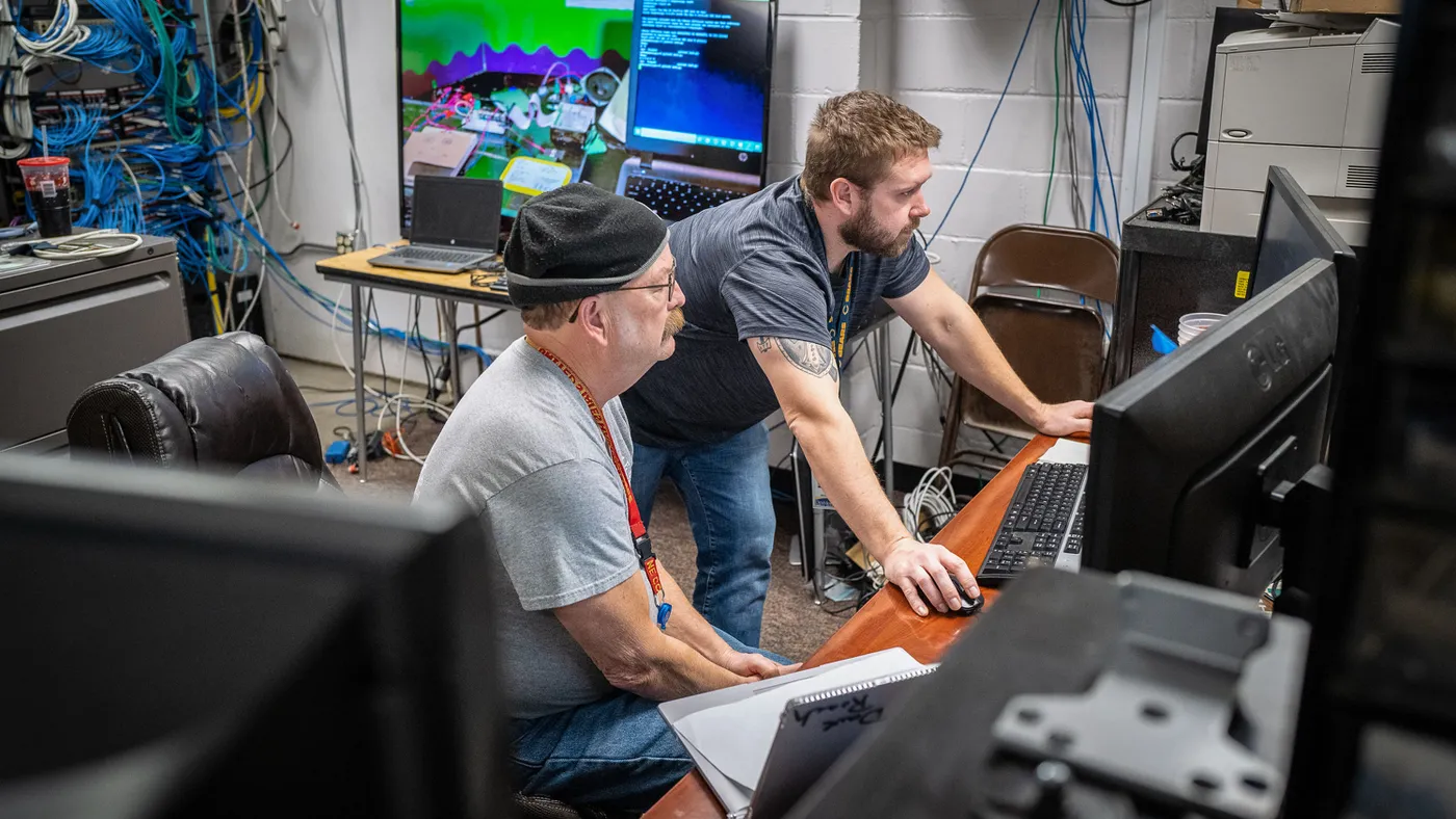 Two IT staff members at Des Moines Public Schools in Iowa are shown working at computers in a server room following a ransomware attack targeting the school district.