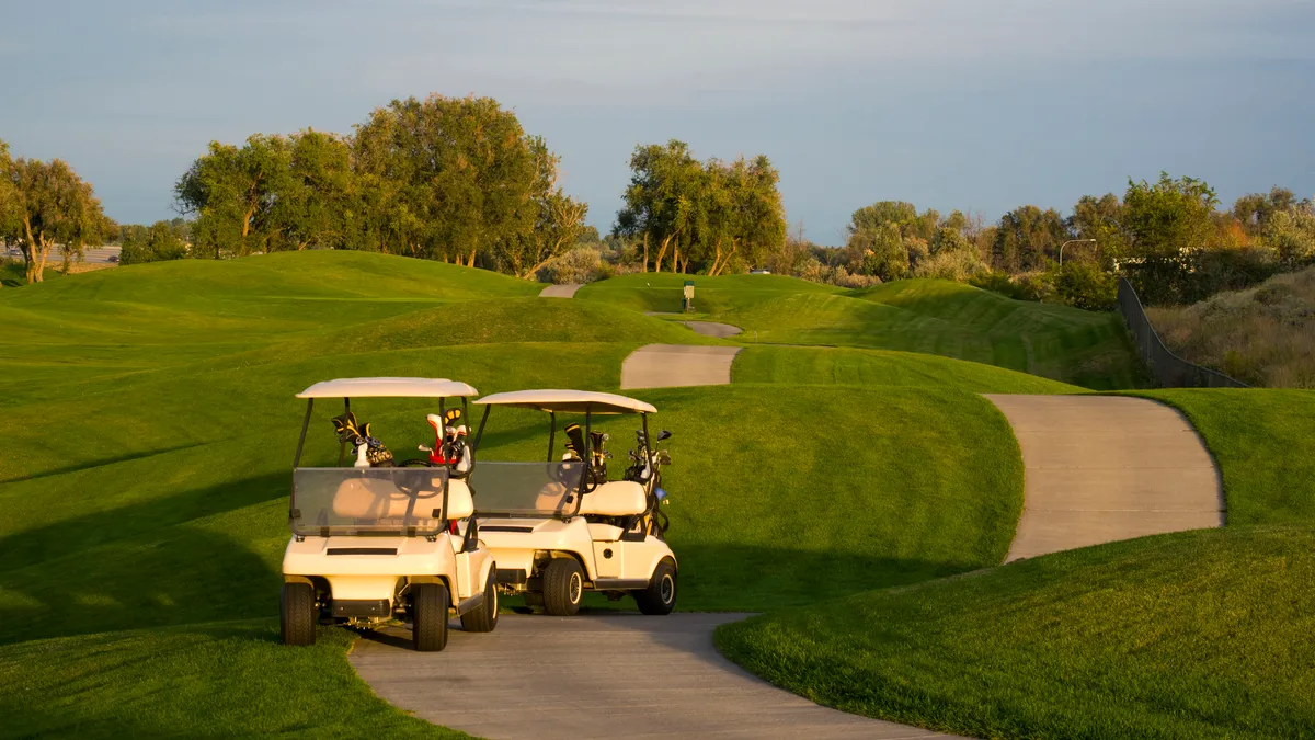 Two golf carts are parked along a drive on a golf course.