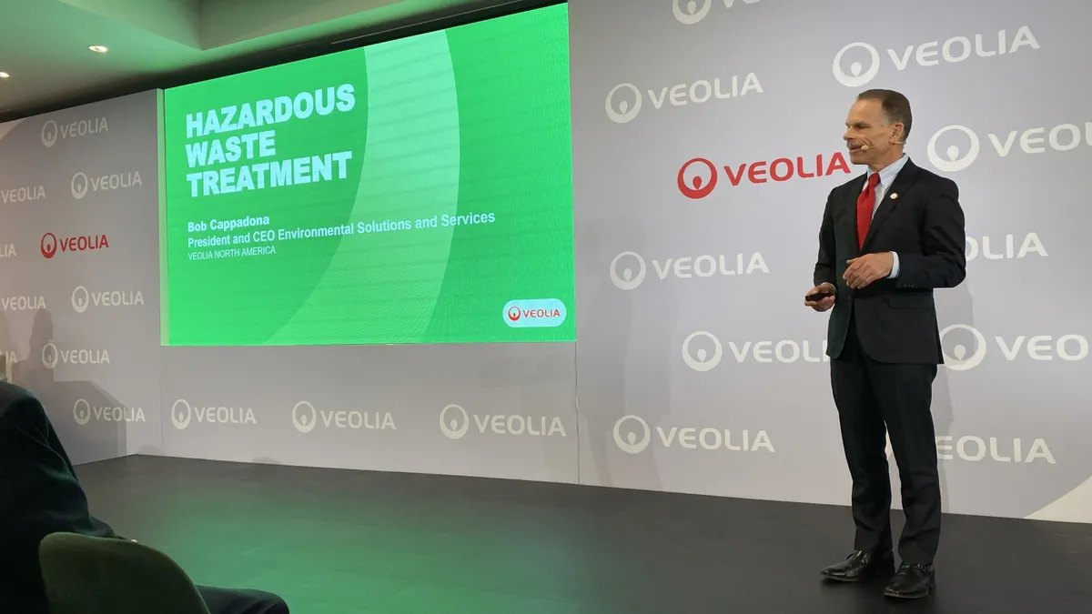 A man stands on a stage in front of a projection screen.