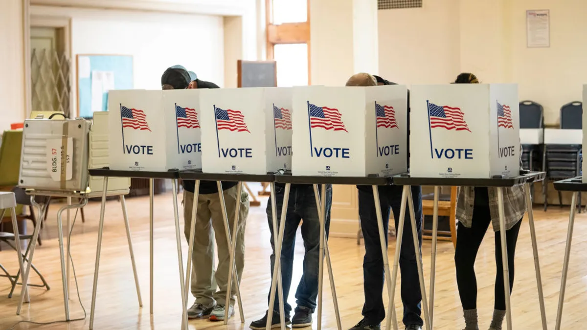 Four voting booths are lined up, filled with people.