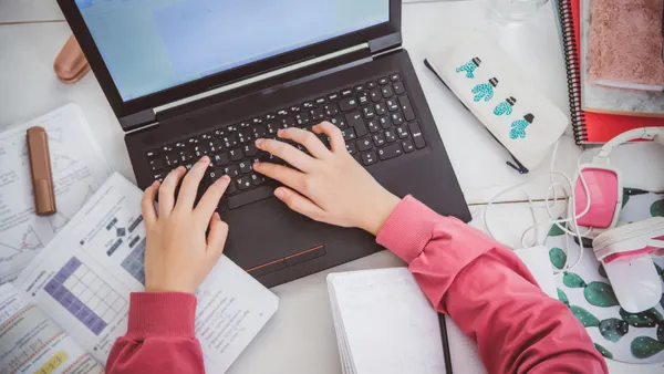 A teenage student studying online while using a laptop at home.