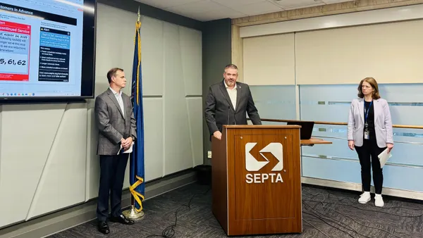 A in a suit standing at podium lettered "SEPTA" with a woman on his left and another man to his right.
