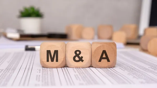 Three wooden cubes spell out m&A, representing business mergers and acquisitions.