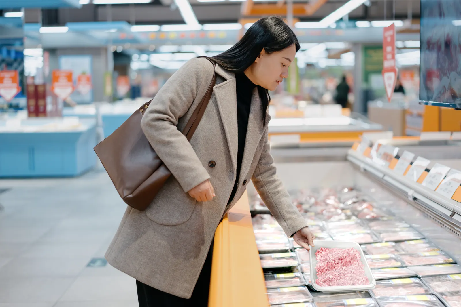 A person in a grocery story holds a tray of meat.