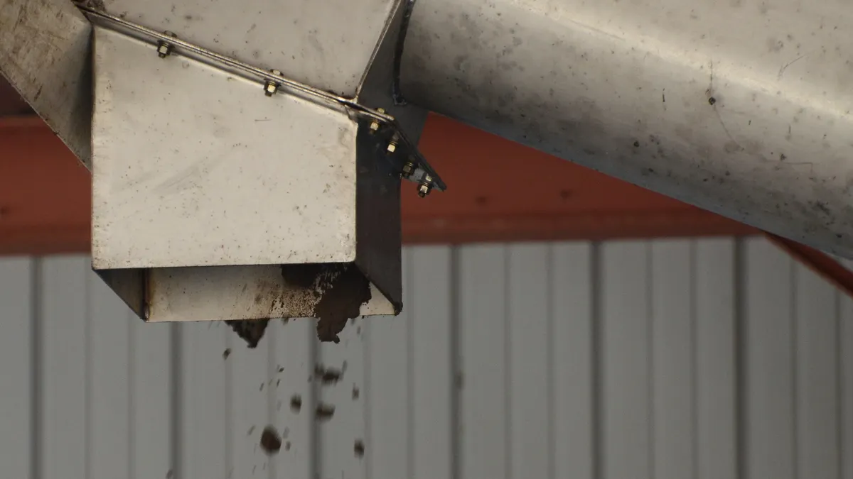 A brown earthy substance falls out of a metal pipe inside a facility.