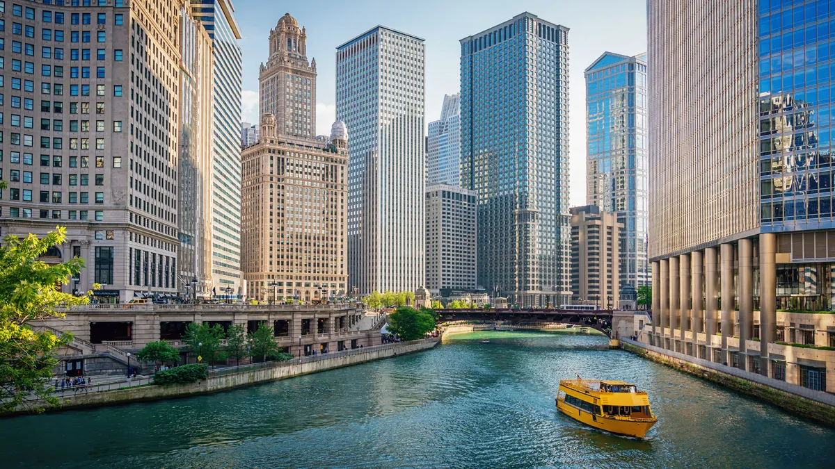 Skyscrapers on either side of a river with a yellow tourboat gliding on it.