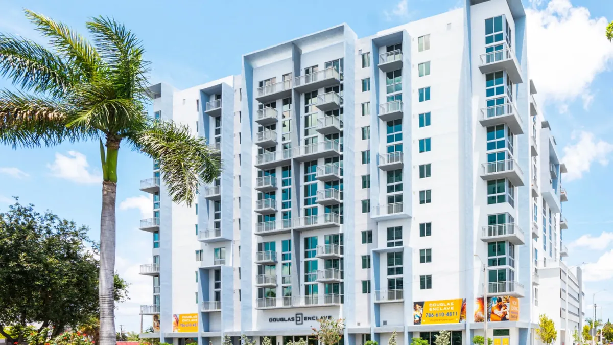 White, high-rise apartment with palm trees and cars in the foreground.