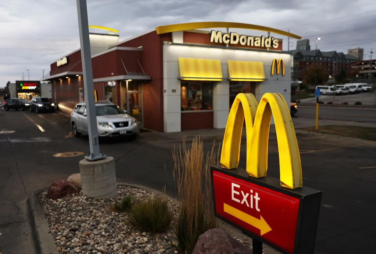 A dawn image of a McDonald&#x27;s drive-thru. At the foreground is an exit sign and there is a car in the background waiting in line.