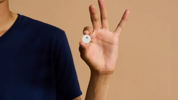 A person holds a round, white device the size of a coin between their pointer finger and thumb.