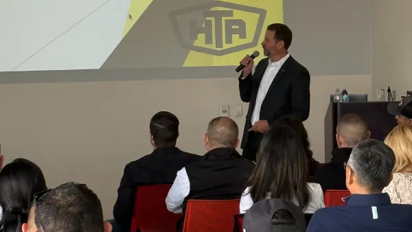 Executive Matt Schrap golds a microphone and speaks in front of a crowd at a conference.