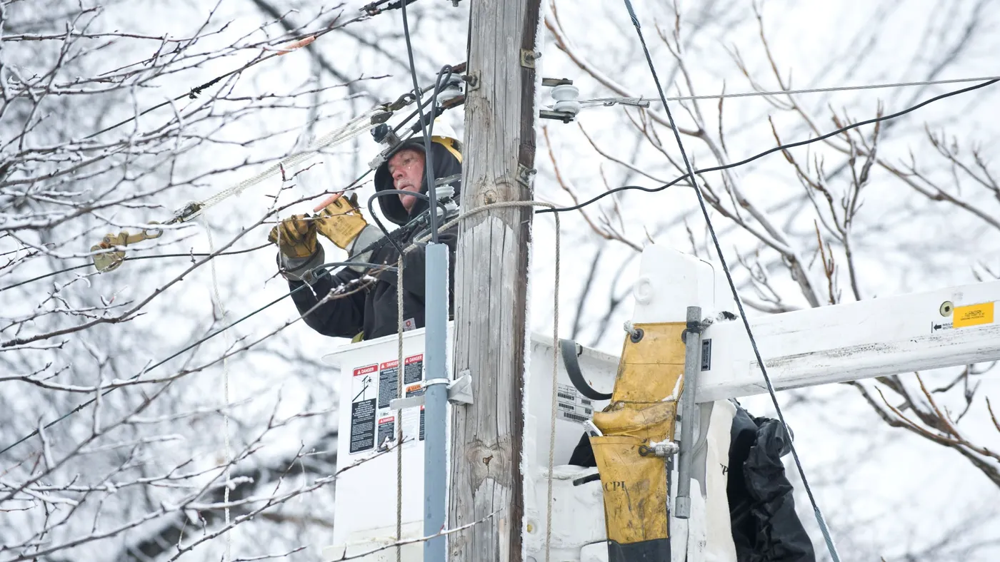 A worker on a utility pole covered in snow and ice.