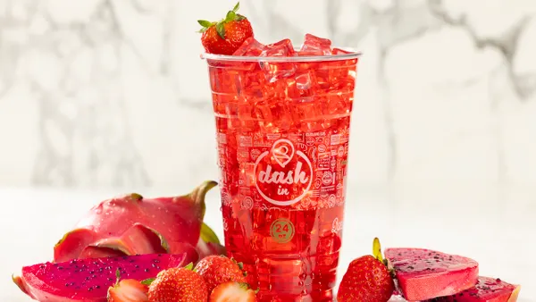 A brightly colored dink in a clear plastic cup sits on a white surface against a white and gray marble background, surrounded by fruit.