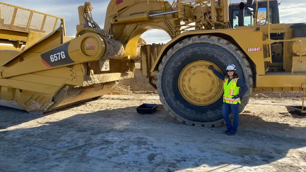 A woman in a hard hat poses in front of a large construction vehicle.