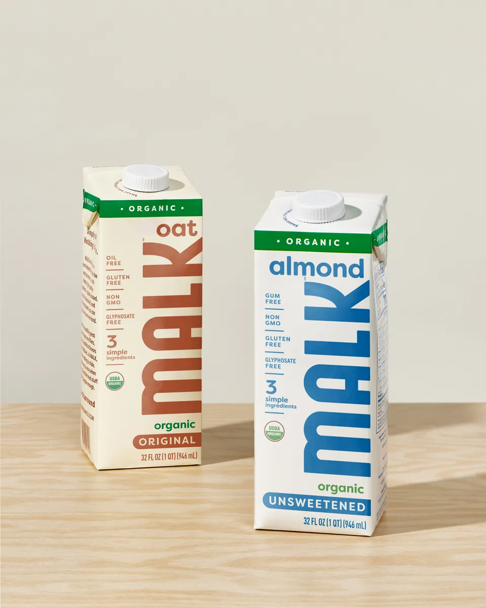 A carton of oat milk next to a carton of almond milk, both with Malk&#x27;s branding on them.