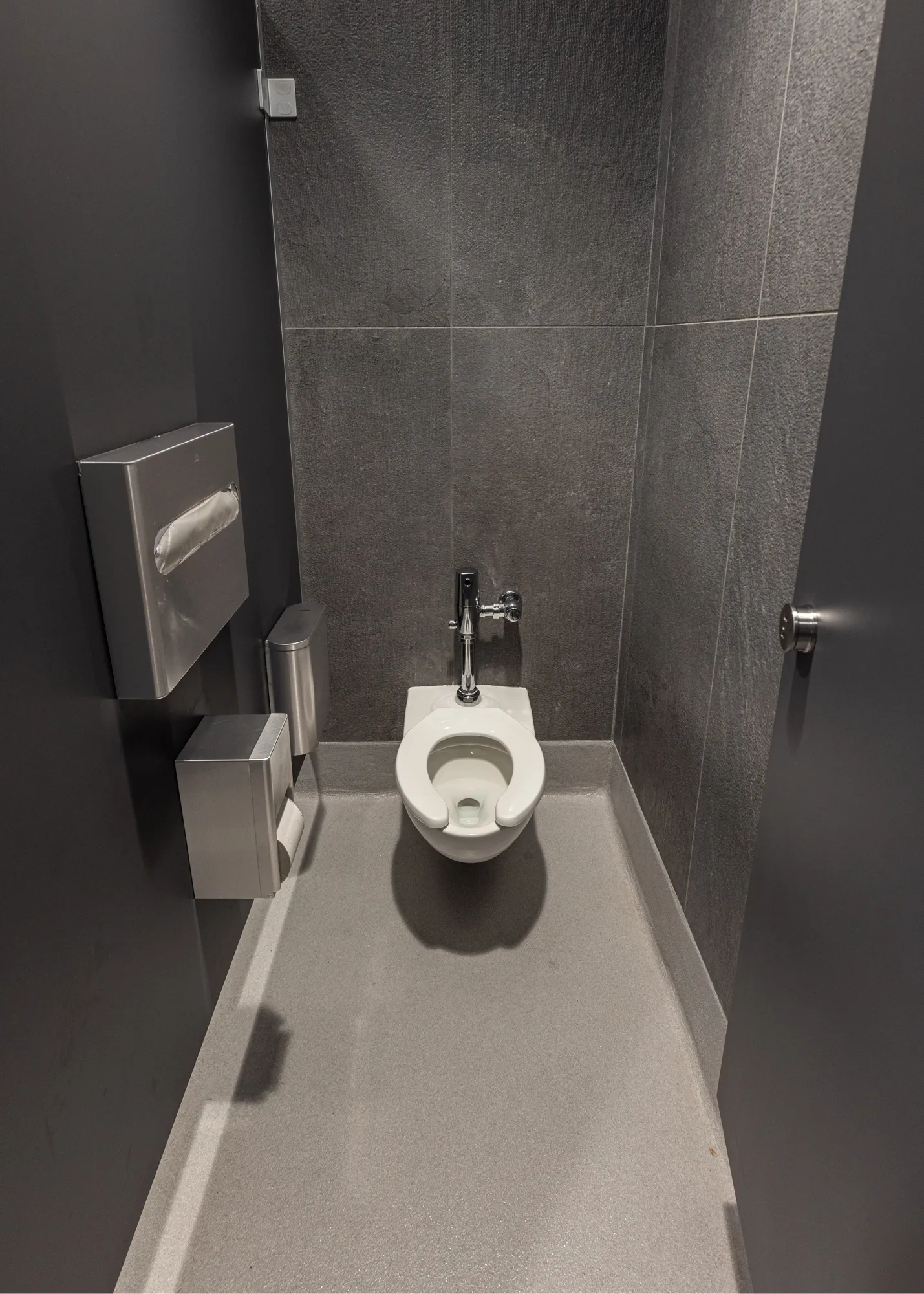 A photo of the interior of a bathroom stall with gray tile and a white toilet.