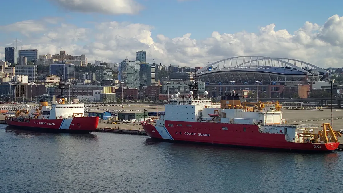 Two large ships are nearby a dock with a city in the background.