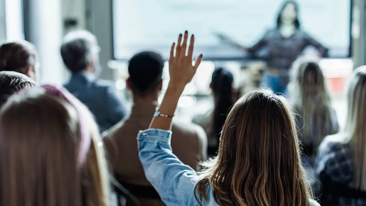 Person raising her hands to ask a question on a seminar in board room.